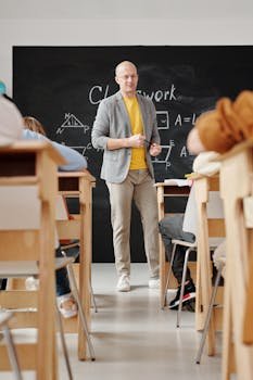 Bald teacher explaining geometry on blackboard to attentive students in classroom.